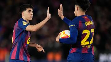 Dw&oacute;ch piłkarzy FC Barcelony w strojach klubowych wykonuje gest "piątki", jeden z nich trzyma piłkę.