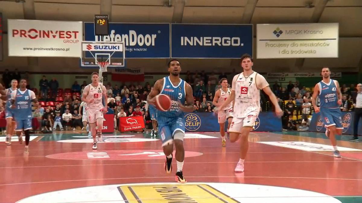 Koszykarze podczas meczu na boisku, jeden z nich prowadzi piłkę.