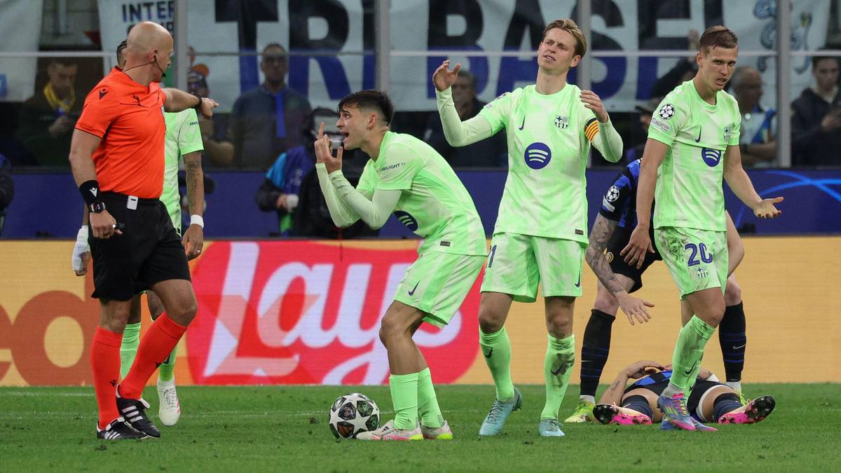 Sędzia w pomarańczowej koszulce i asystenci dyskutują z piłkarzami w zielonych strojach na boisku piłkarskim.