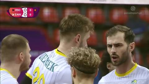 Gracze drużyny siatkarskiej Aluron CMC Warta Zawiercie w białych strojach z żółtymi elementami, rozmawiający ze sobą podczas meczu.