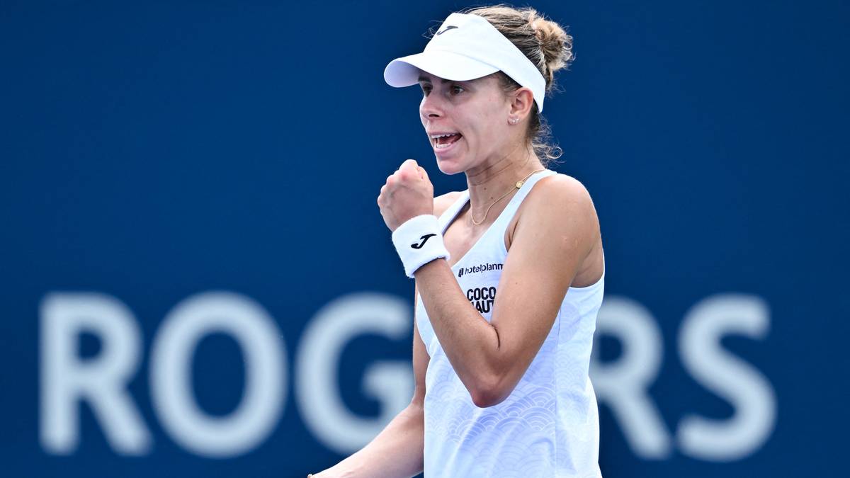 Tenisistka w białej koszulce i białym daszku cieszy się ze zwycięstwa, zaciskając pięść. Na tle niebieska tablica z logo "ROGERS".