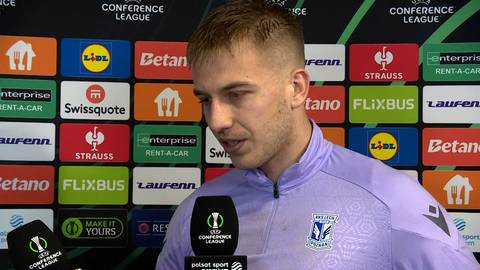 Piłkarz Mateusz Skrzypczak w jasnofioletowej koszulce z herbem Lecha Poznań podczas wywiadu na tle ścianki z logo Ligi Konferencji Europy.