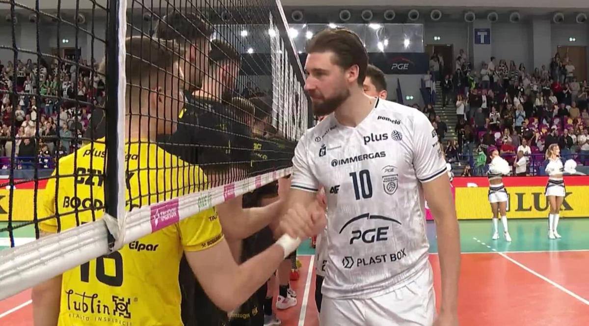 Dwóch siatkarzy po przeciwnych stronach siatki ściska sobie dłonie na znak sportowego ducha rywalizacji.
