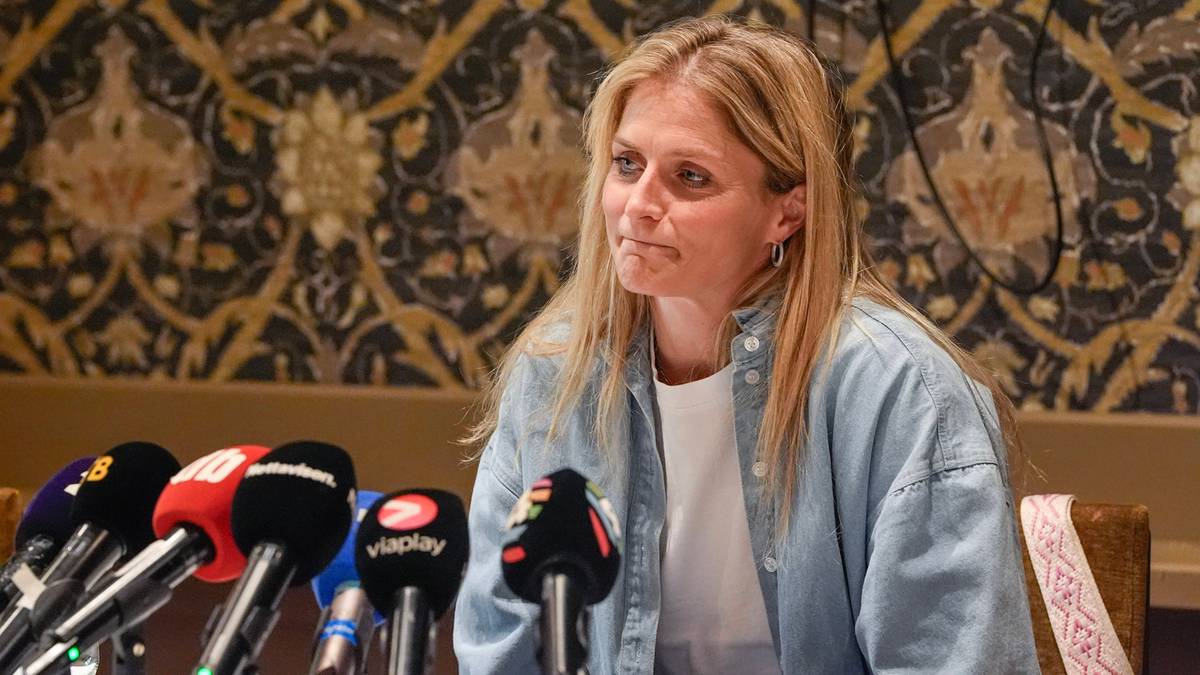 Kobieta z jasnymi włosami w dżinsowej koszuli siedzi przed rzędem mikrofon&oacute;w podczas konferencji prasowej.