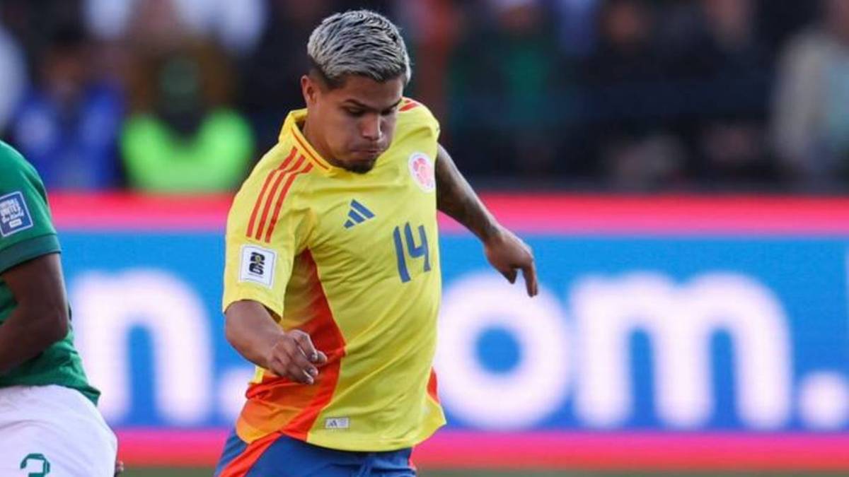 Piłkarz w żółtej koszulce z numerem 14, w ruchu na boisku piłkarskim.