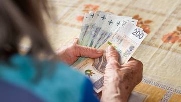 Dłonie starszej osoby trzymające polskie banknoty o nominałach 100 i 200 złotych.