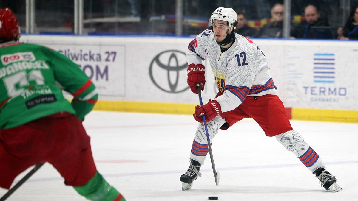 Dw&oacute;ch zawodnik&oacute;w hokeja na lodzie podczas meczu, jeden w białym stroju z numerem 12.