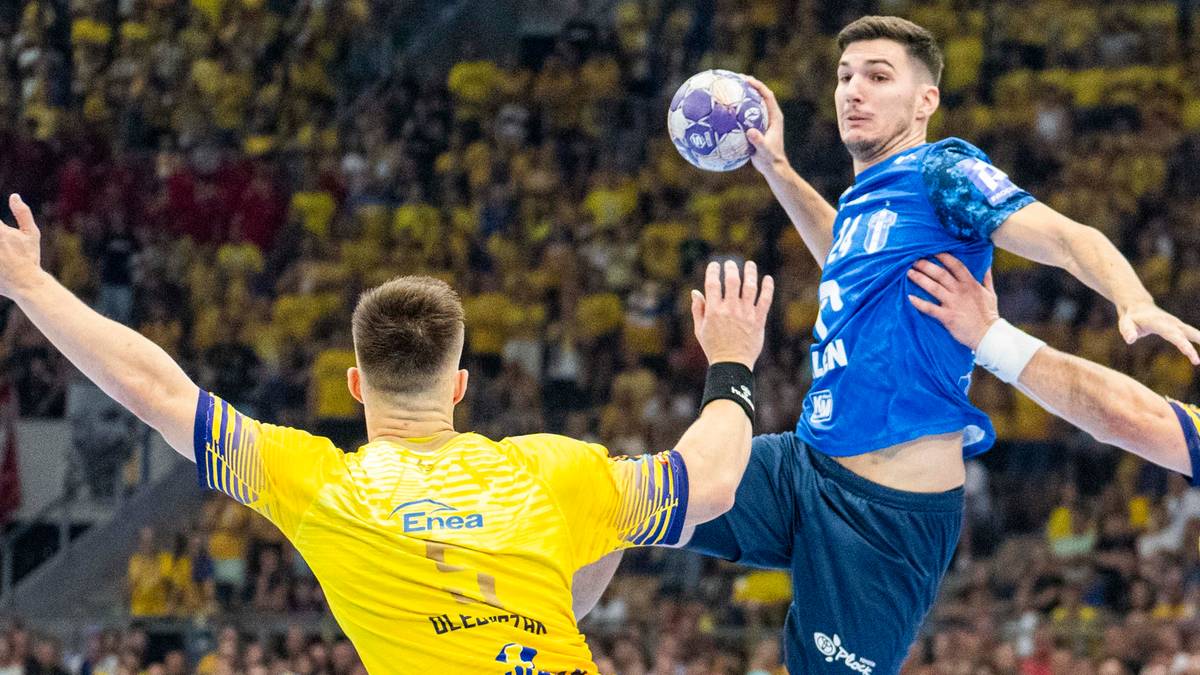 Dwóch zawodników w akcji podczas meczu piłki ręcznej. Jeden w niebieskiej koszulce rzuca piłkę, drugi w żółtej koszulce próbuje go zablokować.