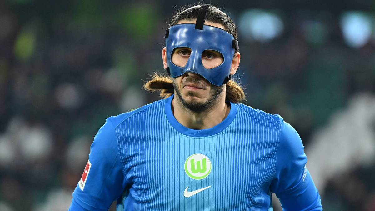 Piłkarz w niebieskiej masce ochronnej na twarzy i niebieskiej koszulce z logo klubu.