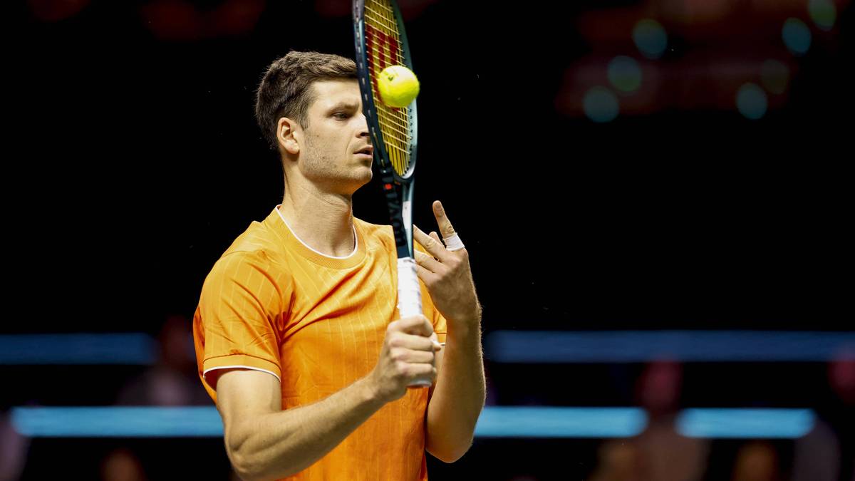 Tenisista Hubert Hurkacz w pomarańczowej koszulce trzyma rakietę tenisową, z piłką odbijającą się od jej naciągu.