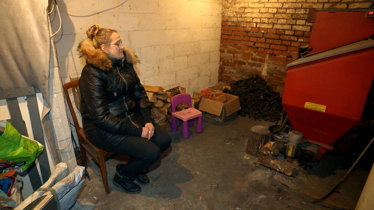 Kobieta siedzi w zimnym pomieszczeniu z piecem i opałami.