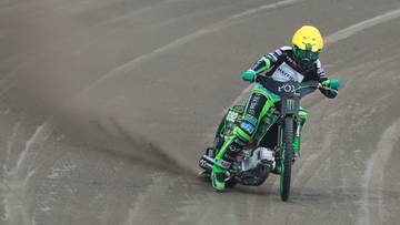 Motocyklista żużlowy w kasku i stroju sportowym ściga się po torze.