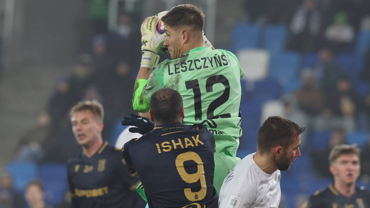 Bramkarz Wisły Płock Rafał Leszczyński w zielonej koszulce z numerem 12 broni strzał, zasłaniając piłkę rękami. Napastnik Lecha Poznań Mikael Ishak w granatowej koszulce z numerem 9 próbuje zdobyć bramkę. W tle widoczni inni piłkarze obu drużyn oraz trybuny stadionu.