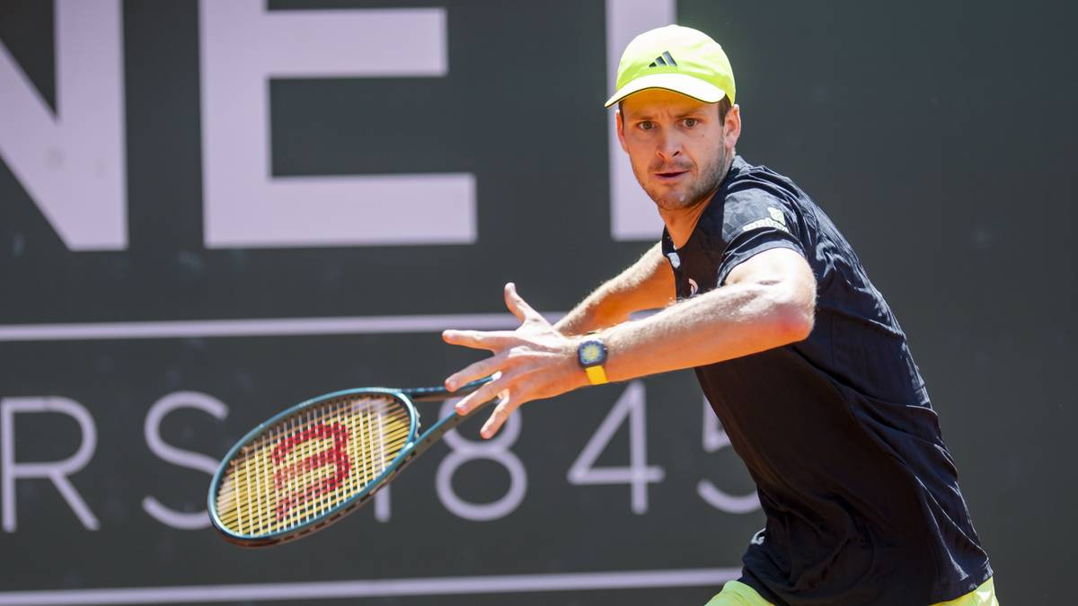 Hubert Hurkacz, polski tenisista, w żółtej czapce z daszkiem i czarnej koszulce, zagrywa piłkę rakietą tenisową podczas meczu.