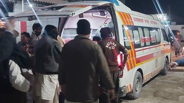 Osoby stoją wok&oacute;ł otwartej karetki pogotowia, z kt&oacute;rej wyciągany jest pacjent.