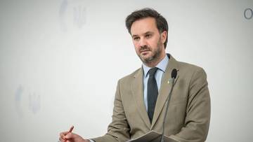 Mężczyzna w garniturze przemawia przy m&oacute;wnicy.