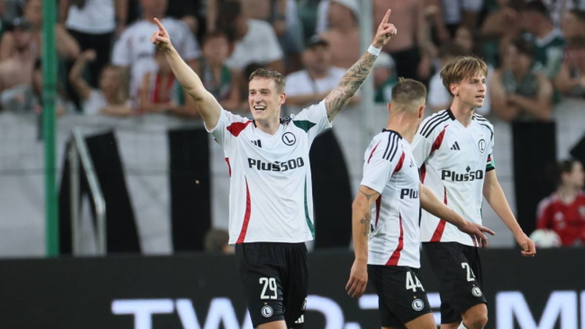 Piłkarz w białej koszulce z numerem 29 i napisem "PLUSA" świętuje zdobycie bramki, wskazując palcem w g&oacute;rę.