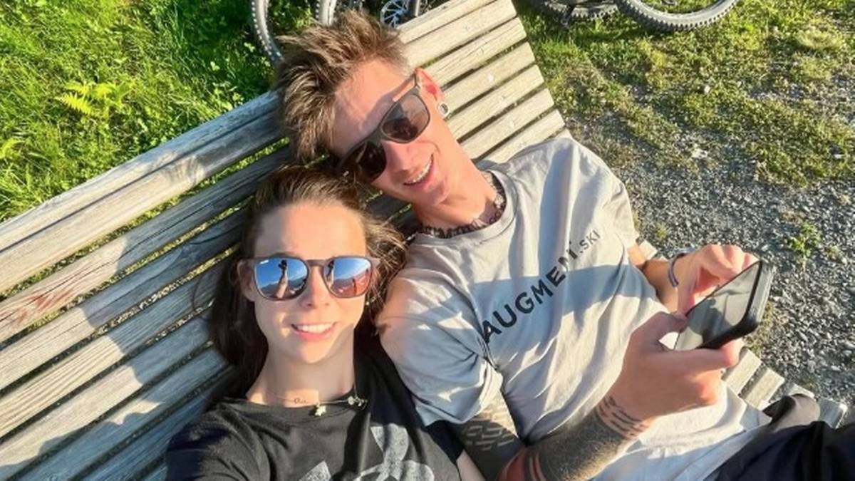 Para siedząca na ławce w słoneczny dzień, mężczyzna trzyma telefon.