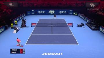 Dw&oacute;ch tenisist&oacute;w grających mecz na korcie tenisowym, jeden przy siatce, drugi na linii końcowej. Wynik meczu wyświetlany na tablicy.