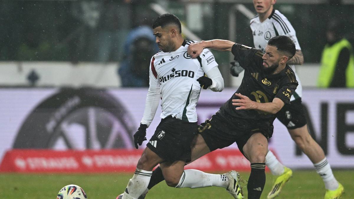 Dwóch piłkarzy rywalizuje o piłkę na zielonym boisku, jeden w białej koszulce z napisem '500', drugi w czarnej.