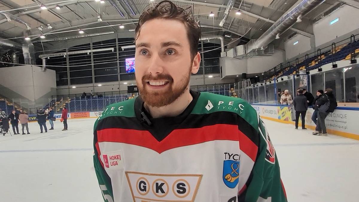 Zawodnik hokeja na lodzie w stroju drużynowym, uśmiecha się do kamery na lodowisku.