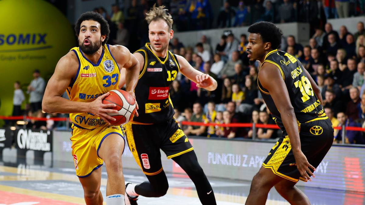 Trzej koszykarze na boisku podczas meczu, jeden z nich prowadzi piłkę, dw&oacute;ch przeciwnik&oacute;w stara się go zatrzymać.