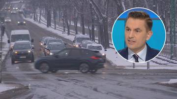 Mężczyzna w garniturze przemawia w k&oacute;łku z niebieskim tłem, obok niego droga zimą z kilkoma samochodami.