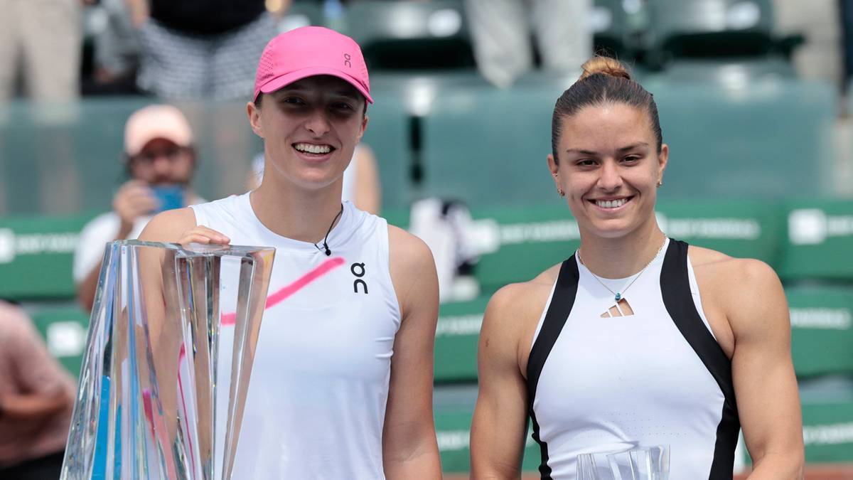 Dwie kobiety w strojach sportowych stoją obok siebie, jedna z nich trzyma dużą przezroczystą statuetkę.