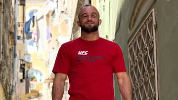 Mężczyzna w czerwonej koszulce UFC stoi na ulicy i uśmiecha się.
