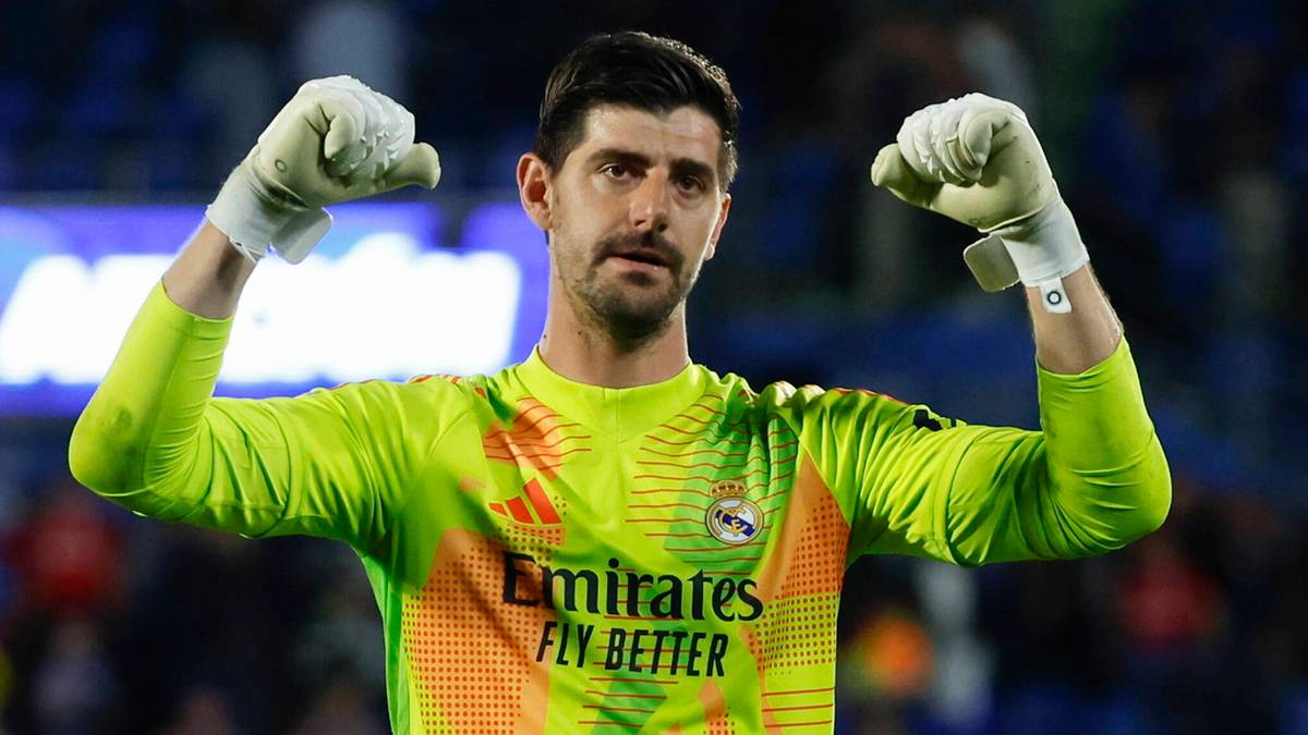 Bramkarz Realu Madryt, Thibaut Courtois, w zielonej koszulce z logotypem "Emirates Fly Better", prezentuje się na tle rozmytej publiczności.