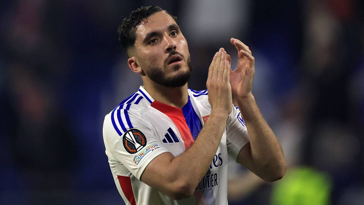 Piłkarz w białej koszulce z niebieskimi i czerwonymi elementami, klaszczący.