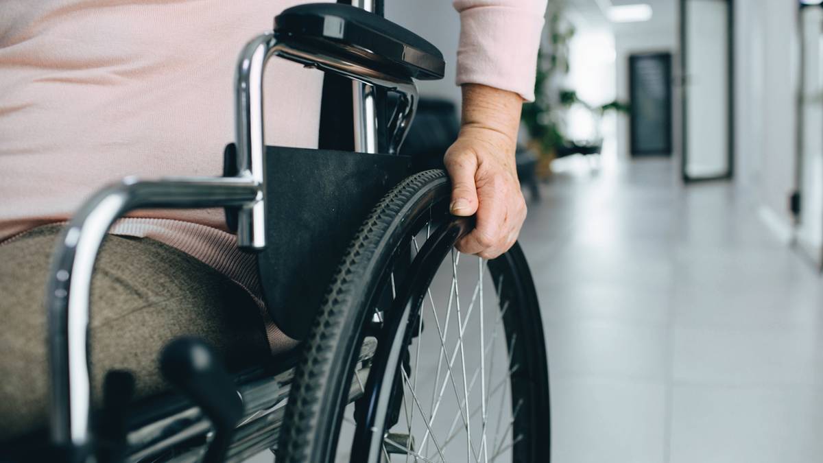 Osoba siedząca na w&oacute;zku inwalidzkim trzyma się za koło.