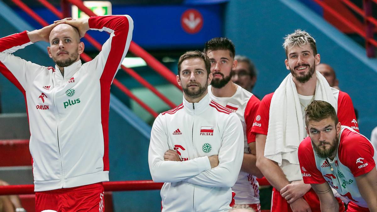 Grupa siatkarzy w strojach sportowych, jeden z nich trzyma się za głowę.