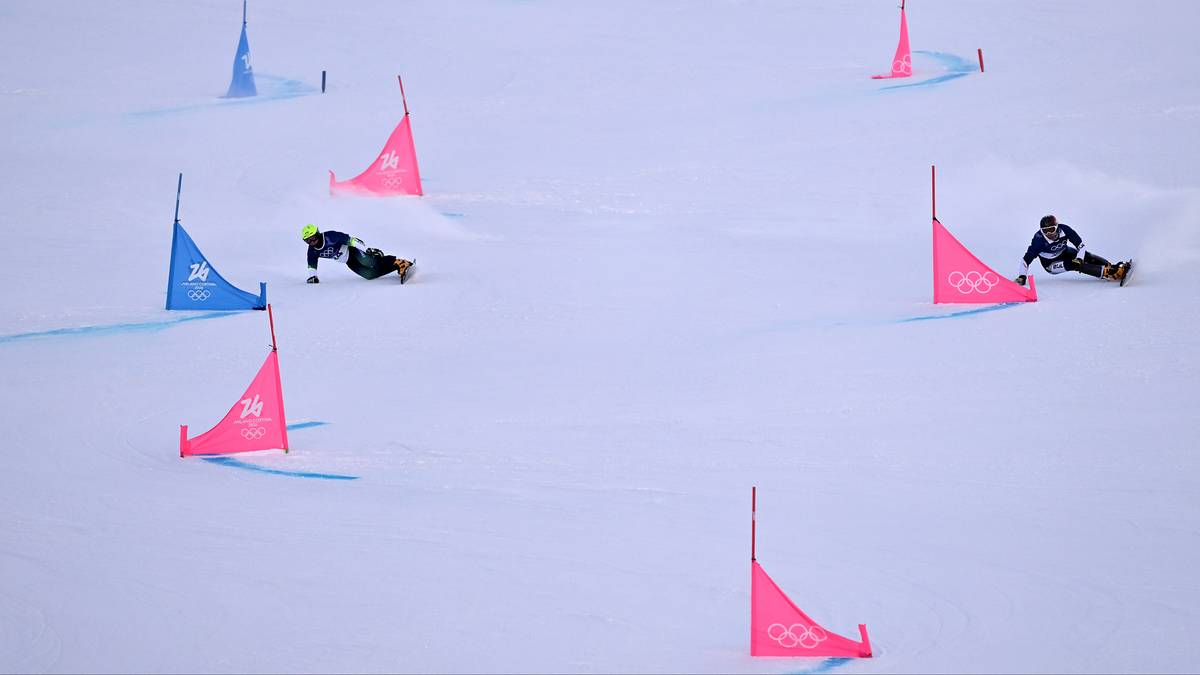 Zawodnicy snowboardu zjeżdżają po stoku narciarskim, omijając r&oacute;żowe i niebieskie tyczki.