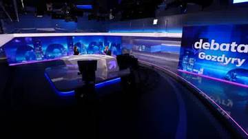 Studio telewizyjne z owalnym stołem, kamerami i monitorami. Na jednym z ekran&oacute;w widnieje napis "debata Gozdyry".