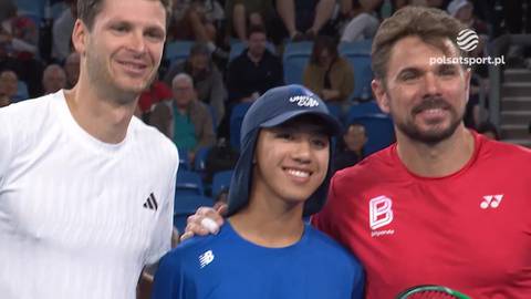 Hubert Hurkacz i Stan Wawrinka stoją obok siebie, uśmiechając się, z młodym chłopcem pomiędzy nimi na korcie tenisowym.