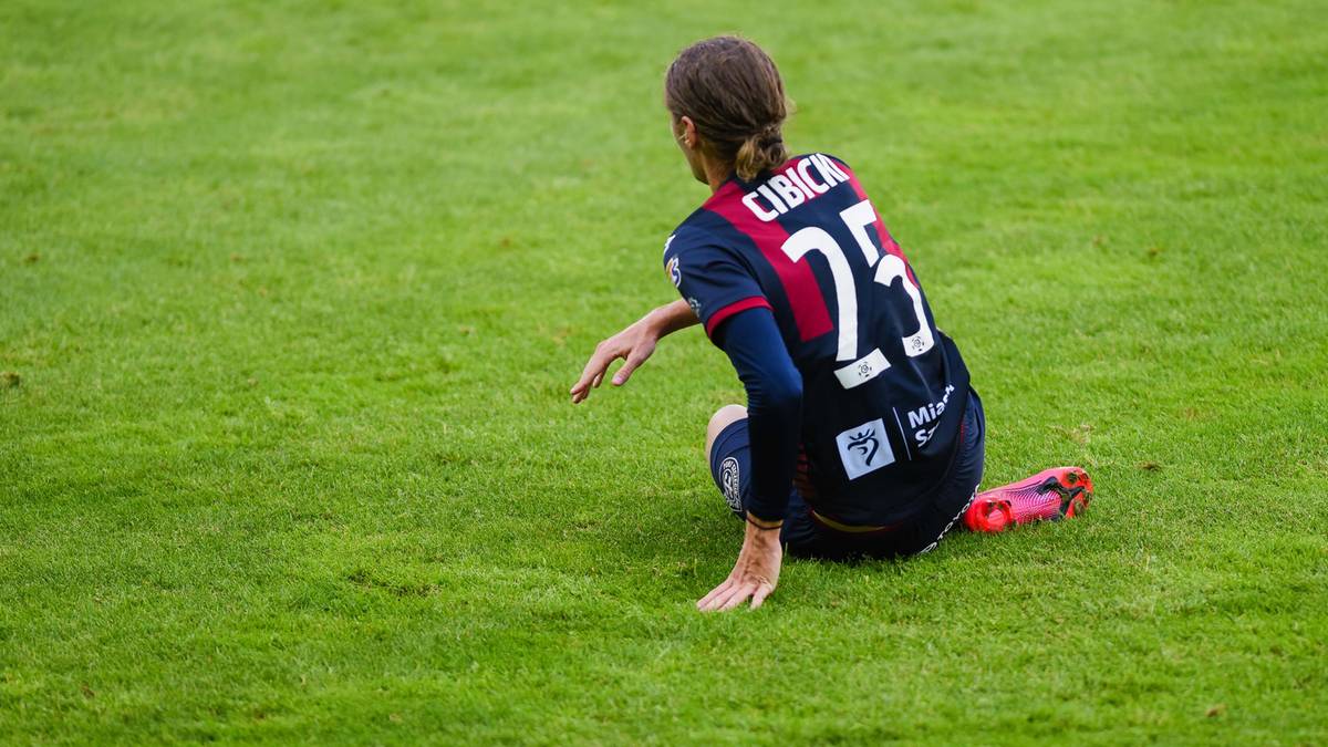 Piłkarz w koszulce z numerem 25 kuca na zielonej murawie stadionu.