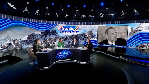 Cztery osoby siedzą przy stole w studiu telewizyjnym. Na ekranie za nimi widoczne są elementy graficzne związane ze sportami zimowymi i g&oacute;rami. Po prawej stronie znajduje się czarno-białe zdjęcie mężczyzny.