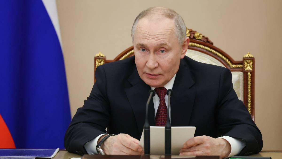 Władimir Putin siedzi przy stole z dokumentami i mikrofonem.