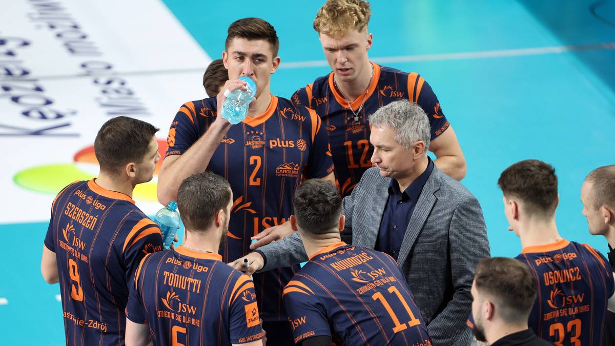 Grupa siatkarzy w niebiesko-pomarańczowych strojach, z których jeden pije wodę z butelki.