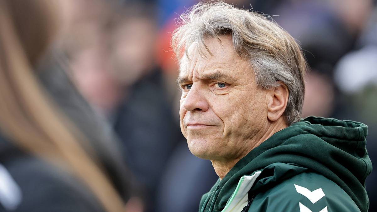 Portret mężczyzny w średnim wieku z siwiejącymi włosami, ubranego w zieloną bluzę z kapturem z białymi symbolami na ramieniu.