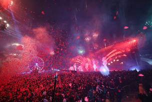 Tłum ludzi ogląda nocny pokaz sztucznych ogni i świateł nad sceną podczas finału WOŚP.
