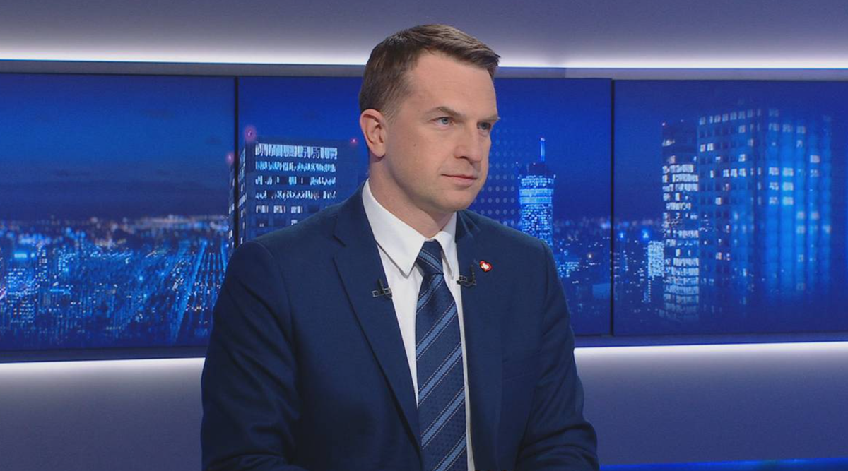 Mężczyzna w garniturze siedzi przed ekranami z widokiem na nocne miasto.
