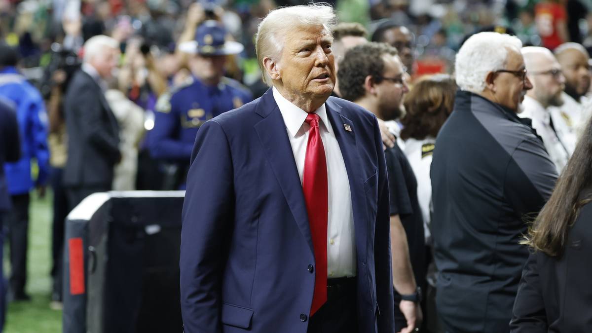 Donald Trump w garniturze i czerwonym krawacie, otoczony ludźmi na trybunach.