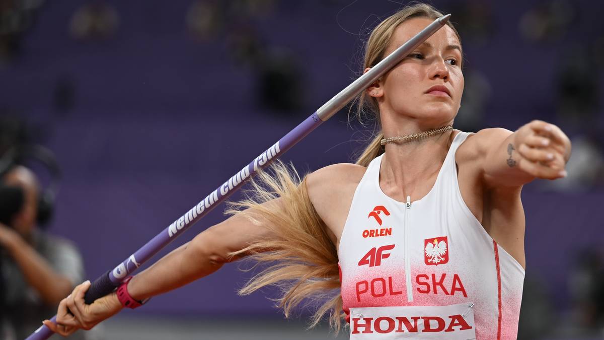 Atletka w białej koszulce z napisem "POLSKA" i numerem startowym rzuca oszczepem na zawodach.