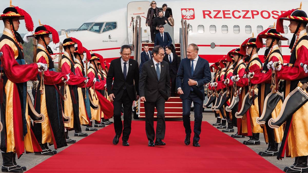 Premier Donald Tusk i przedstawiciele Korei Południowej na czerwonym dywanie przed samolotem.
