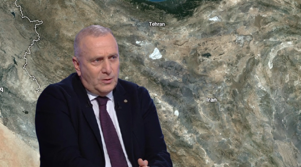 Mężczyzna w garniturze siedzi na tle mapy Bliskiego Wschodu z zaznaczonym Iranem.