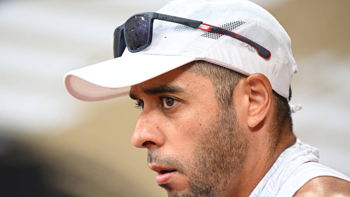 Mężczyzna w białej czapce z daszkiem, na której oprawione są okulary przeciwsłoneczne, z uwagą patrzy w bok.