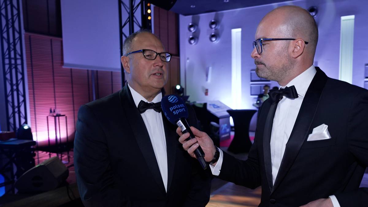 Dwóch mężczyzn w garniturach, jeden z nich udziela wywiadu do mikrofonu z logo Polsat Sport.