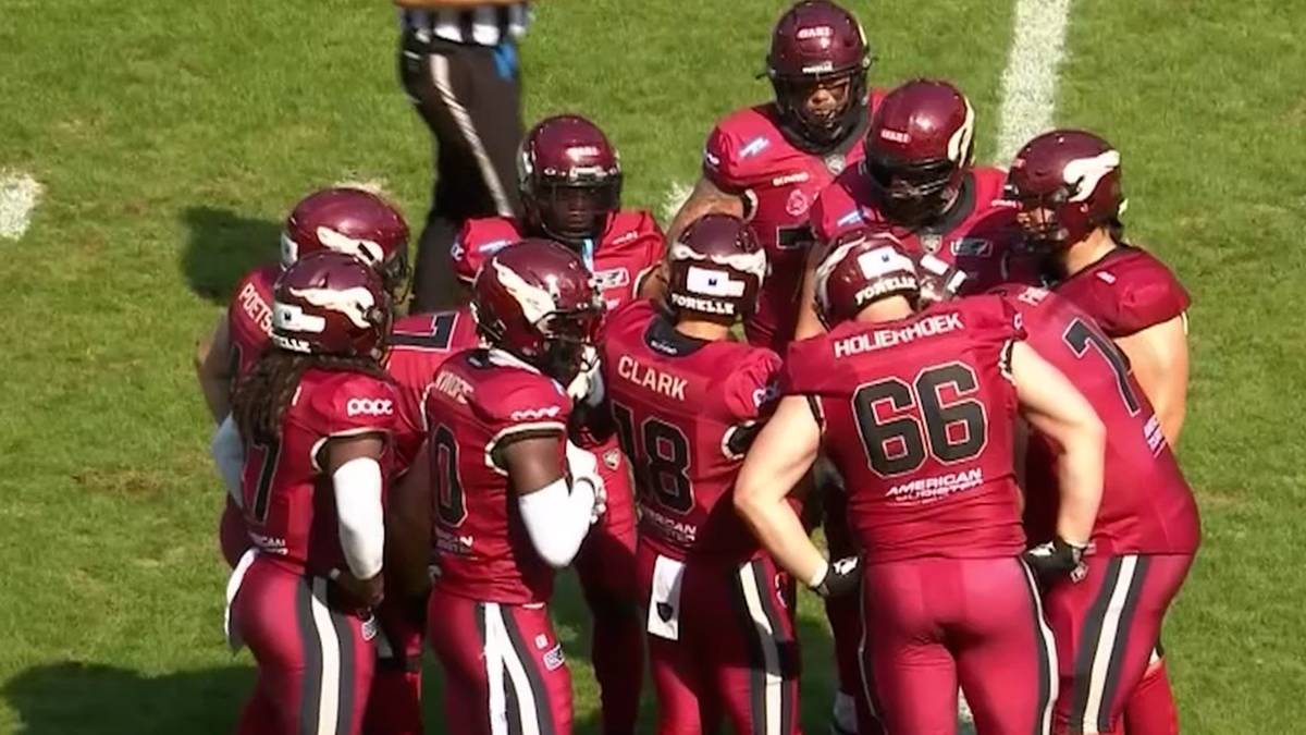 Drużyna graczy futbolu amerykańskiego w czerwonych strojach i kaskach zebrana w środku pola.